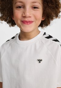 T-shirt en coton blanc avec un emblème de abeille noire et des accents d'épaules noirs à motifs contrastants. Texture lisse avec une coupe décontractée.