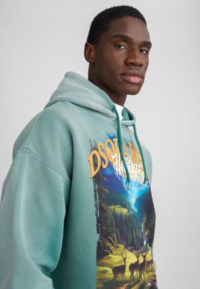 Light green hoodie with a front graphic depicting a forest scene, featuring deer. Hood has adjustable drawstrings and a relaxed fit.