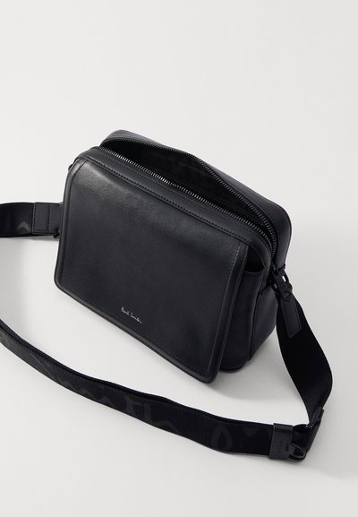 Borsa a tracolla in pelle nera con chiusura a zip, superficie liscia e tracolla regolabile con un'accents a motivo. Logo sulla parte anteriore.