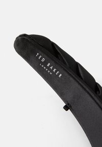 Čierny saténový čelenka s prešívaným dizajnom. Obsahuje jemné logo "TED BAKER" vytlačené na bielo. Navrhnuté pre pohodlie a štýl.