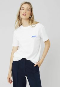 T-shirt en coton blanc avec le texte bleu "MORE Pleasure" sur la poitrine gauche. Col rond et manches courtes, associé à un pantalon navy.