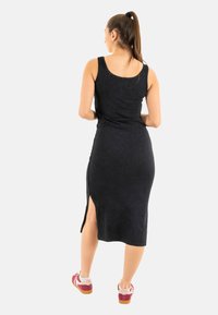 Vestido midi negro sin mangas con un diseño ajustado y una abertura lateral. Textura suave, patrón minimalista, combinado con zapatillas deportivas que tienen detalles en rojo y blanco.