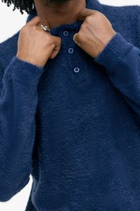 Navy blue, fuzzy texture pullover with a buttoned collar. Features subtle buttons and long sleeves, emphasizing a soft and cozy appearance.