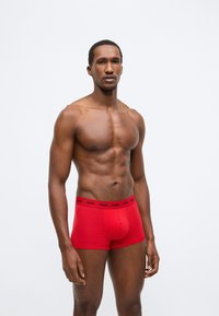 Piros pamut boxeralsó testhezálló fazonban. Fekete derékpánttal, logó részletekkel. Simap felületű, kényelmet és tartást biztosító kialakítás.