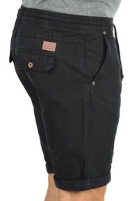 Pantalones cortos negros hechos de una tela ligera con una cintura elástica, bolsillos laterales y dobladillos enrollados. Presenta una etiqueta de parche en la parte posterior.