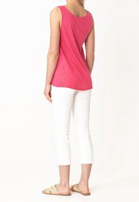 Top senza maniche di colore rosa con vestibilità rilassata, texture morbida e orlo posteriore arrotondato, abbinato a pantaloni bianchi a tre quarti e sandali piatti intrecciati.