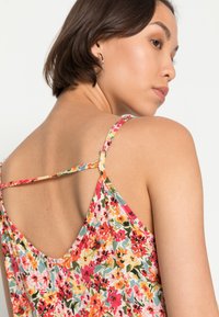 Camisola com padrão floral, apresentando cores vibrantes, alças finas e um design de costas baixas. O material parece leve e de textura suave.