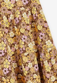 Vestido de tela floral en tonos marrones, amarillos y lavanda, con un diseño plisado que presenta flores distintivas y una textura suave.