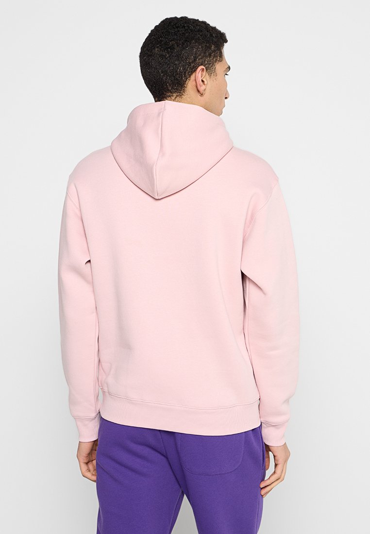 Sweat-shirt à capuche rose avec une coupe décontractée, fabriqué en tissu doux. Il possède une grande capuche et des poignets côtelés, accompagné d'un pantalon violet.