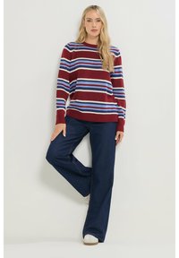 Bordeaux gebreide trui met horizontale blauwe en witte strepen, gecombineerd met donkerblauwe wijde jeans en witte sneakers.