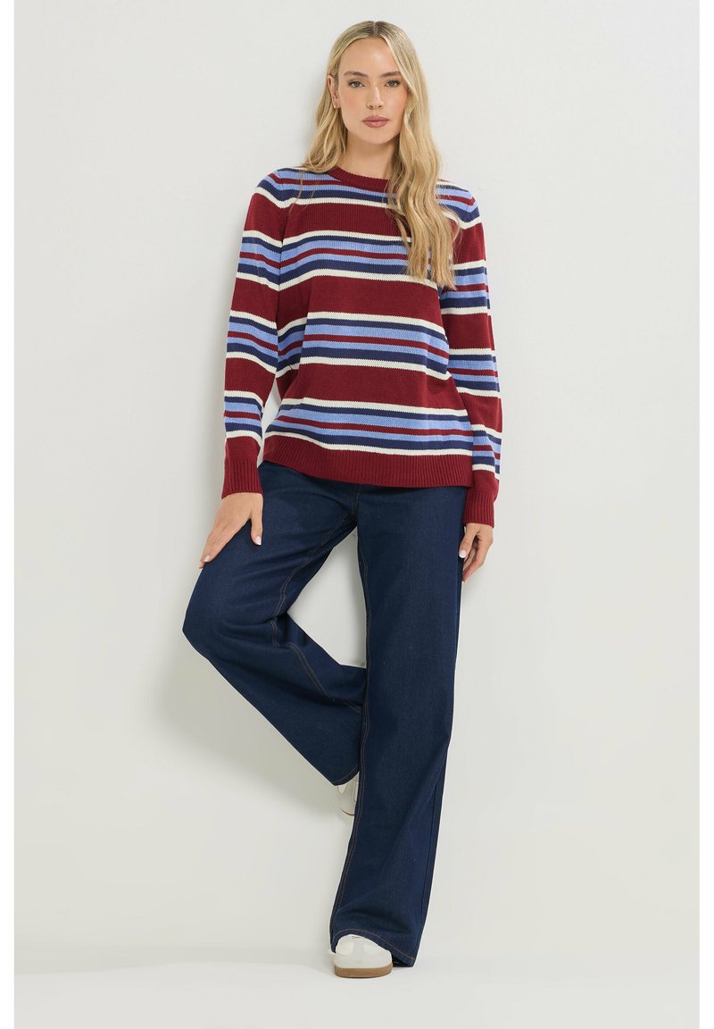 Bordeaux gebreide trui met horizontale blauwe en witte strepen, gecombineerd met donkerblauwe wijde jeans en witte sneakers.