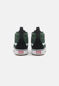 Sneakers alte caratterizzate da una combinazione di suede verde scuro e nero, striscia laterale bianca e suola in gomma con marchio rosso sul tallone.