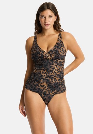 Femme portant un haut tankini imprimé léopard et un bas de bikini assorti, posant avec une main sur la hanche devant un fond uni.