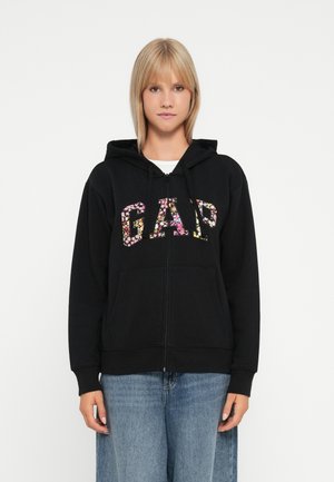 Črna zip-up kapuca z rožnatim logotipom "GAP", dvema sprednjima žepoma in kapuco z vrvico. Mehka, srednje težka tkanina.