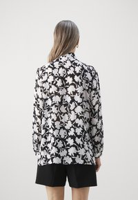 Svart och vit blomsterblus med lång ärm, i genomskinligt material, rundad krage och samlade manschetter, matchad med svarta shorts.