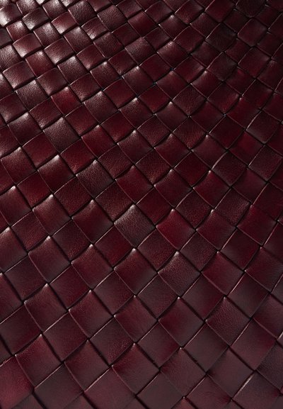 Burgundijas krāsas āda ar austu rakstu, kas satur kvadrātveida tekstūras, radot trīsdimensiju efektu virsmā.