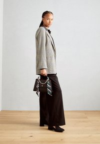 Blazer a cuadros grises sobre una camisa negra, pantalones anchos negros y bailarinas negras, sosteniendo un pequeño bolso negro con detalles de cadena y cinta.
