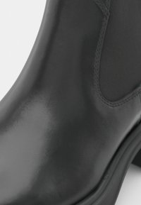 Svart läderankelboot med en slät yta, elastiska sidopaneler, rund tå och en robust gummisula.