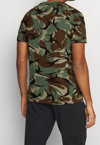 Katoenen t-shirt met korte mouwen, met een camouflagepatroon in groene, bruine en zwarte tinten, ronde halslijn en een zachte textuur.