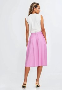 Różowa spódnica z wysokim stanem i plisami, o gładkiej, lekkiej teksturze oraz ukrytym zamkiem z tyłu, zestawiona z białym topem bez rękawów.