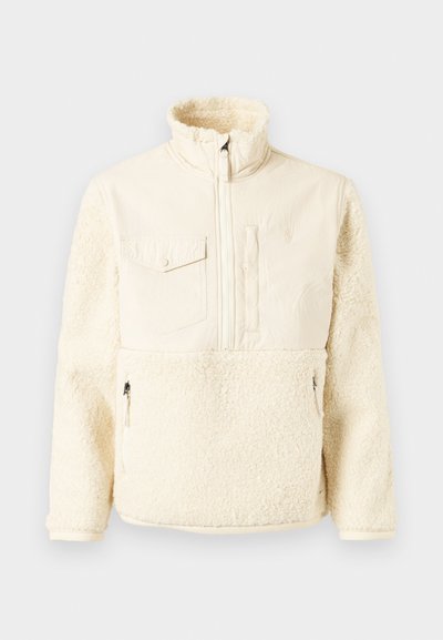 Casaco pullover de cor creme com uma parte inferior suave e fofinha, tecido superior liso, gola alta, fecho frontal e um bolso no peito.
