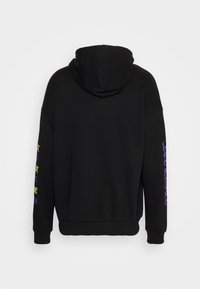 Black hoodie made from soft fabric, featuring a hood and ribbed cuffs. The left sleeve displays colorful purple and green text design.