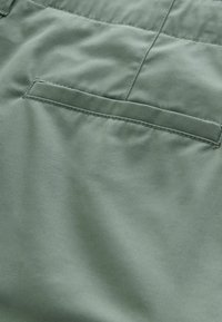 Gros plan sur une poche arrière en tissu vert avec des coutures nettes sur un vêtement, mettant en valeur la texture et les coutures.