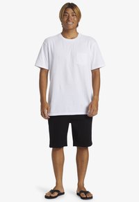 White short-sleeve t-shirt with a chest pocket, paired with black shorts and black flip-flops. Casual fit, cotton material.