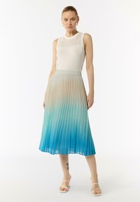 Gonna plissettata con una sfumatura ombré da beige a blu, realizzata in tessuto leggero. Abbinata a una canotta bianca aderente e sandali con cinturini.