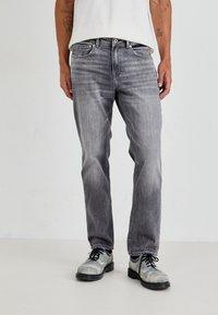 Γκρι τζιν παντελόνι με ίσια γραμμή, ξεθωριασμένη απόχρωση, πέντε τσέπες και αντίθετες ραφές, συνδυασμένο με γκρι κορδονάτα παπούτσια.