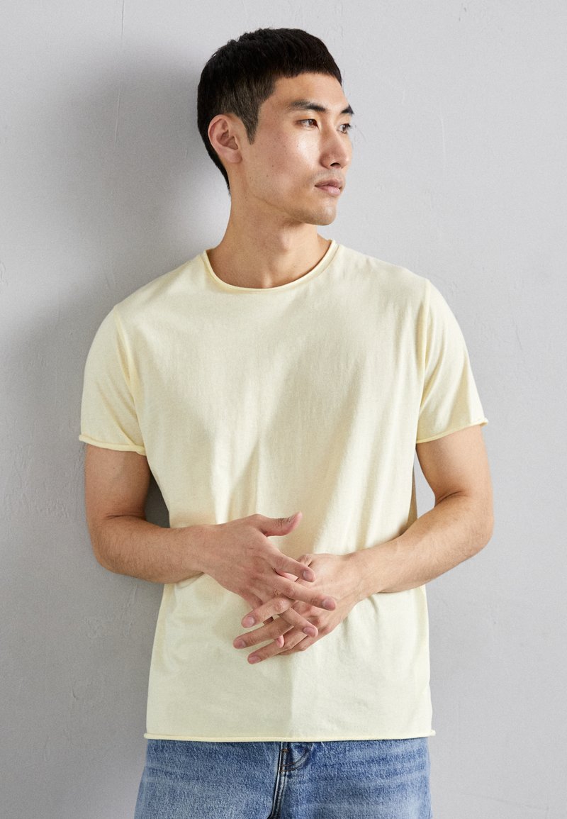 T-shirt jaune clair à manches courtes en coton doux, col rond, avec une coupe décontractée. Porté avec un jean en denim bleu.