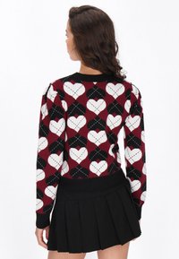 Roter und schwarzer Pullover mit Herzmuster, ausgestattet mit einem gerippten Rundhalsausschnitt und Bündchen, kombiniert mit einem schwarzen Faltenrock.