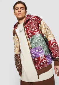 Multicolored bomber jacket with intricate paisley patterns in red, green, purple, and beige, featuring a front zipper and brown ribbed cuffs.