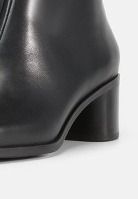 Musta nahast pahkluu saabas, sileda viimistlusega, kontuurse disainiga ja tugev plokk-kontsaga. Peen tikkimine mööda servi.