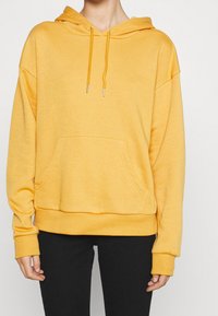 Sweat à capuche jaune en tissu doux, avec une poche frontale, une capuche à cordon de serrage, et des poignets et ourlet côtelés. Coupe décontractée et détails minimalistes.