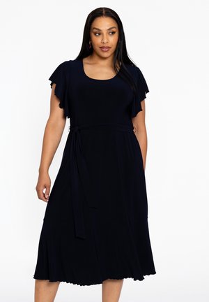Ein marineblaues Kleid aus weichem Stoff, mit kurzen Rüschensäumen, einer taillierten Taille und einem ausladenden, gewellten Saum.