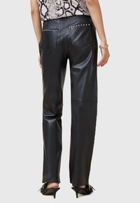 Zwarte leren broek met een gladde textuur, voorzien van gestifte accenten op de achterzakken, een recht model en een lichte glans.