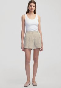 Beige geplooide shorts met een hoge tailleband en zijzakken, gecombineerd met een aansluitend wit tanktop. Gladde stof en casual ontwerp.