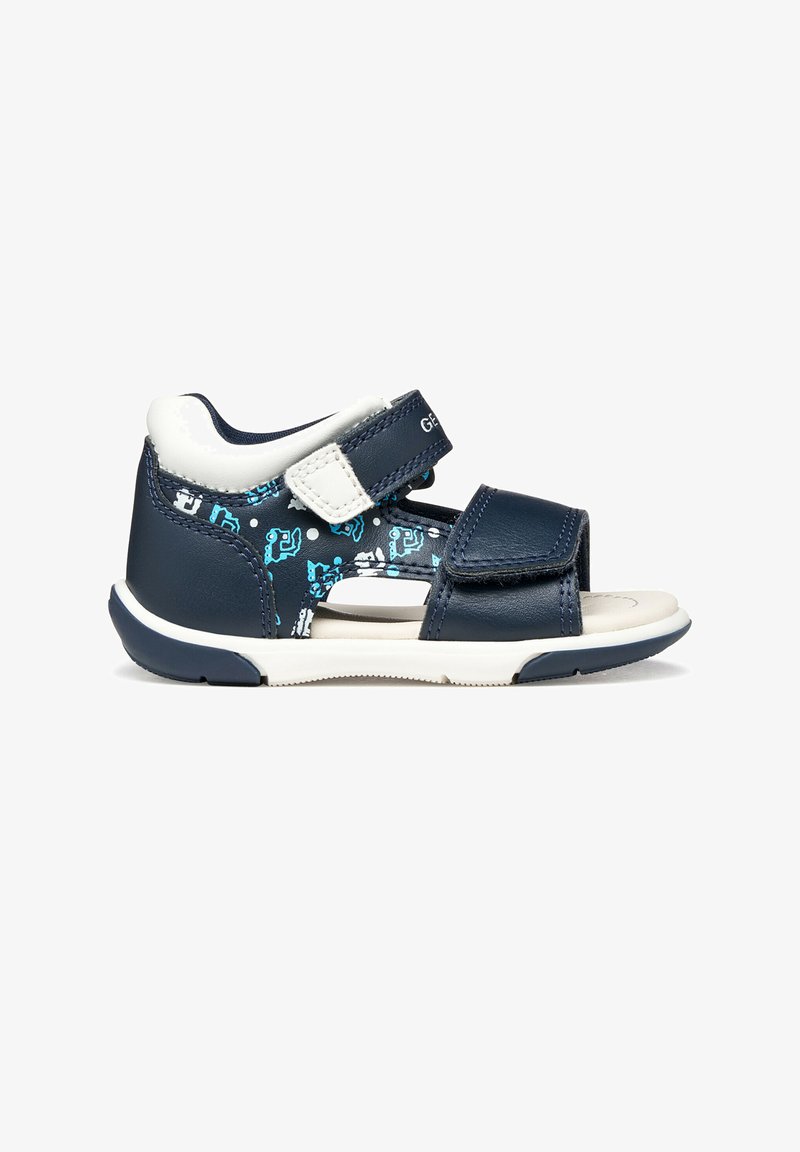 Sandales bleu marine avec accents blancs, bandes Velcro réglables, découpes, et un motif avec des détails bleu clair. Semelle en caoutchouc.