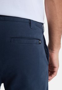 Pantalones azul marino con una textura suave, que presentan un bolsillo trasero con una pequeña etiqueta de logo y un diseño de cintura estándar.