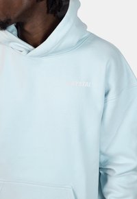 Lichtblauwe hoodie met een zachte textuur, voorzien van een kenguruzak en het woord "CRYSTAL" in het wit gedrukt op de borst.