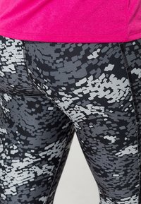 Svart och grå mönstrade tights med en digital kamouflage-design och en rosa topp. Tyget är elastiskt med synliga sömmar.