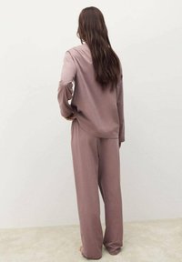 Ensemble de loungewear léger et doux en mauve ; haut ample à manches longues avec un col rond et un pantalon à jambes larges. Texture de tissu lisse.