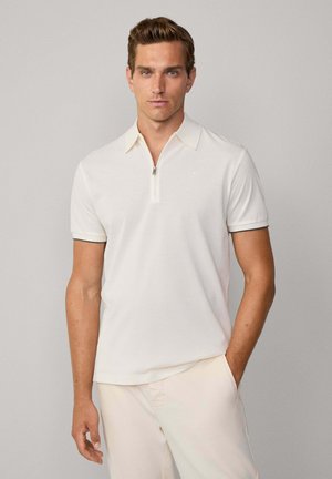 Hellbeige Polo-Shirt mit Reißverschlusskragen, kurzen Ärmeln und subtilen Kontrastdetails. Der Stoff wirkt glatt und hat einen schlanken Schnitt.