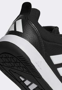 Chaussure de sport noire avec dessus en cuir texturé et mesh. Accents blancs sur le talon et la semelle présentant un motif de bande de roulement pour l'adhérence et la durabilité.