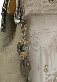 Beige strukturierte Ledertasche mit geprägten Mustern und dekorativen Metallakzenten. Enthält einen Anhänger mit einer Katze, einen Schlüsselanhänger und verschiedene Verzierungen.