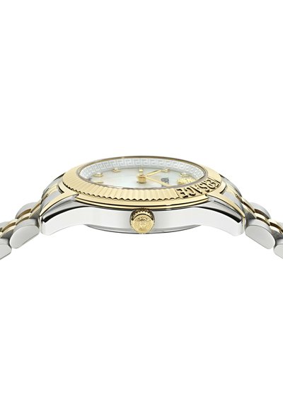 Reloj de acero inoxidable con un bisel dorado, esfera blanca, marcadores de hora dorados y una pulsera bicolor. Presenta un logotipo en la corona.