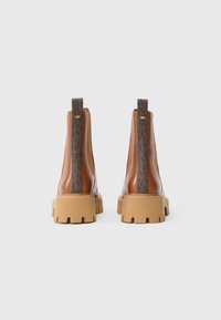 Bottes basses en cuir marron avec un panneau texturé à motif, une semelle beige épaisse et un passant à l'arrière. Détails contrastants sur les côtés.