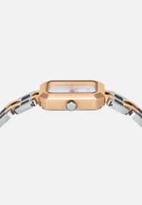 Obdĺžnikové hodinky s ružovo-zlatým a strieborným kovovým remienkom. Majú biely ciferník s ružovo-zlatými akcentmi a bočnú korunku na úpravy.