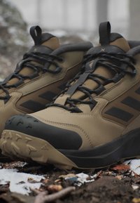Braune und schwarze Wanderschuhe mit profilierten Sohlen, die auf verschneitem, matschigem Boden im Freien liegen.